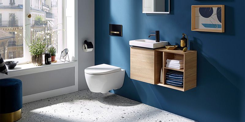 Ein Ausschnitt von einem Badezimmer mit einer blauen Wand. Im Fokus eine Toilette mit Wandhalterung und ein Waschtisch mit Spiegel.
