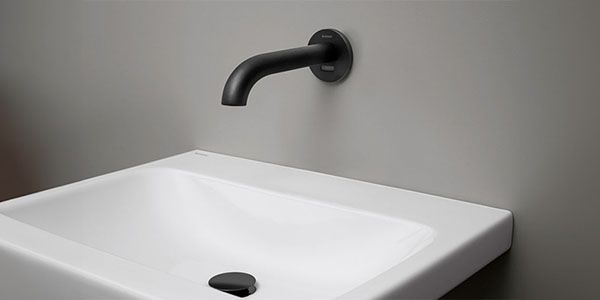 Ein schwarzer Wasserhahn der aus der Wand kommt und einen Bewgungssensor hat.
